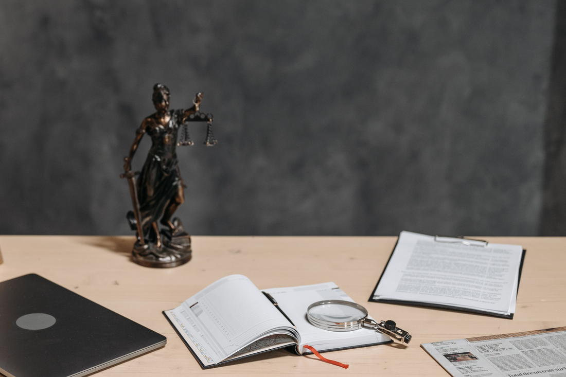 Mesa de trabalho com processo impresso, livro aberto e estatueta da Justiça