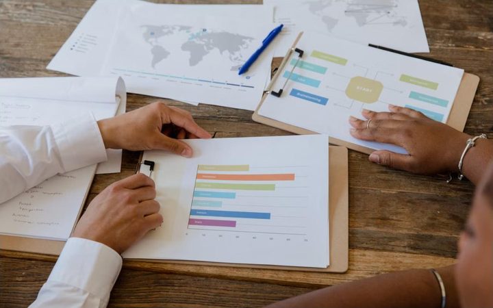 Duas pessoas analisando gr&aacute;ficos impressos sobre a mesa