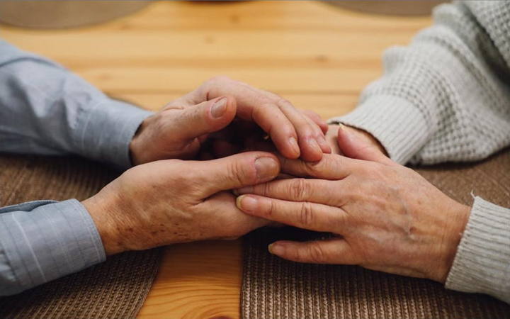 Mãos de um casal idoso unidas sobre a mesa